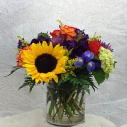 Mixed bouquet with a sunflower, roses, and purple flowers in a glass vase