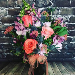 Bouquet of coral roses and purple flowers in a black vase with a ribbon