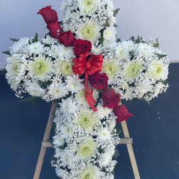 Cross-shaped floral tribute with white flowers and red roses on a stand