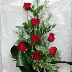 Tall arrangement of red roses in a black vase with greenery