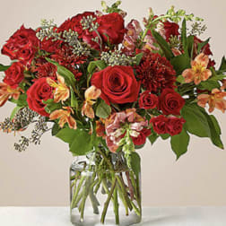 Red roses and mixed blooms arranged in a clear glass vase
