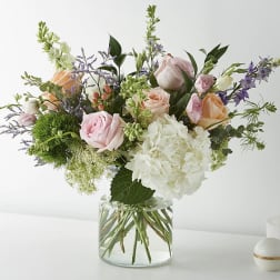 Mixed bouquet of pink and peach roses with white hydrangea in a glass vase