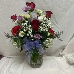 Mixed bouquet of red roses, white blooms, and purple flowers in a glass vase