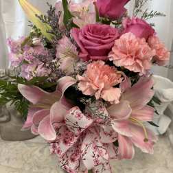 Pink roses, lilies, and carnations in a glass vase with a floral ribbon