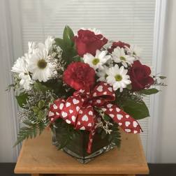 Red roses and white daisies in a glass vase with a heart ribbon