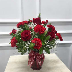 Red roses and carnations in a red glass vase with a patterned ribbon