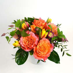 Orange and pink roses with yellow tulips in a white vase