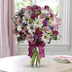 Mixed bouquet of daisies, roses, and pink flowers in a glass vase