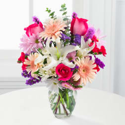 Mixed pink, white, and purple flowers in a clear glass vase