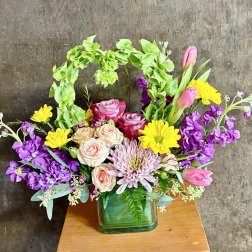 Mixed bouquet in a green glass vase with pink, yellow, and purple flowers