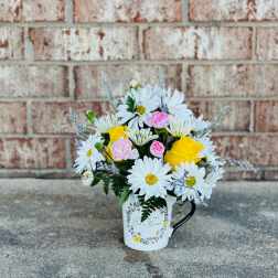 Bouquet of white daisies and yellow and pink roses in a white mug vase