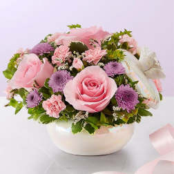 Pink roses and purple daisies arranged in a white bowl vase
