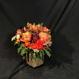Orange and red mixed flower arrangement in a textured vase
