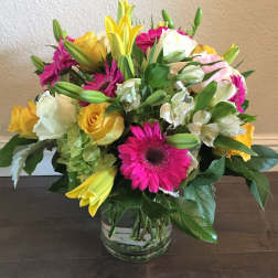 Mixed bouquet of roses, lilies, and gerbera daisies in a glass vase