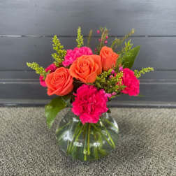 Orange roses and hot pink carnations in a clear glass vase