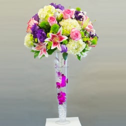 Tall bouquet of pink roses, lilies, and purple flowers in a clear vase