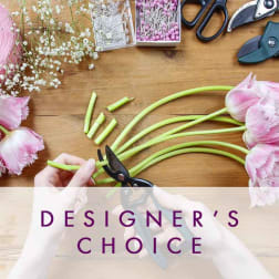 Pink tulips being trimmed on a wooden table with scissors and floral supplies