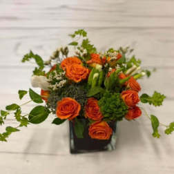 Orange roses arranged in a black square vase with greenery