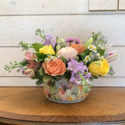 Mixed bouquet in a floral tin container with pink, yellow, and lavender blooms