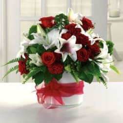 Red roses and white lilies arranged in a clear vase with a red ribbon
