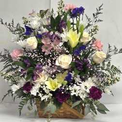 Basket arrangement of roses, lilies, carnations, and daisies in white, purple, and pink