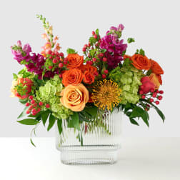 Colorful bouquet of roses, hydrangeas, and snapdragons in a clear glass vase