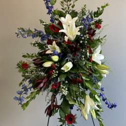 Tall floral spray with white lilies, red blooms, and blue flowers on a stand