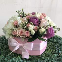 Round pink hatbox of white, blush, and lavender roses with a satin bow on a green textured surface