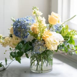 Blue hydrangeas and pale yellow roses in a clear glass vase