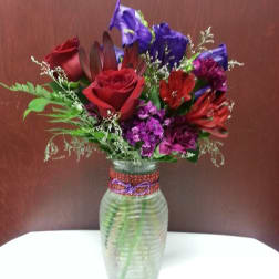 Mixed bouquet of red, purple, and blue flowers in a glass vase