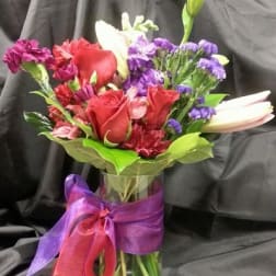 Mixed bouquet of red roses, lilies, and purple flowers in a glass vase