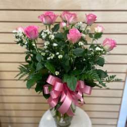 Pink roses arranged in a clear glass vase with a pink ribbon bow