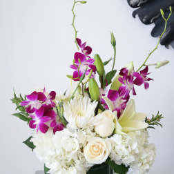 White hydrangeas, roses, lilies, and purple orchids in a green glass cube vase