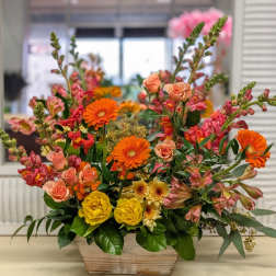 Mixed bouquet in a wooden planter with orange, pink, and yellow flowers