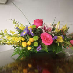 Colorful mixed flower arrangement with roses, lilies, and snapdragons in a low container