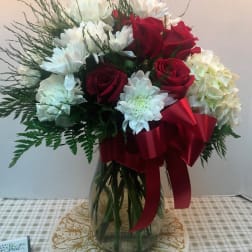 Bouquet of red roses and white flowers in a glass vase with a red ribbon