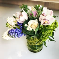 Mixed bouquet with orchids, roses, and blue flowers in a glass vase