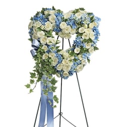 Heart-shaped floral wreath of white roses and blue flowers on a stand