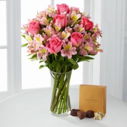 Pink roses and alstroemeria in a clear glass vase with a chocolate box