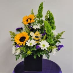 Sunflowers and daisies in a black container with a small bee decoration