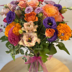Mixed bouquet of orange, purple, and pink flowers in a glass vase