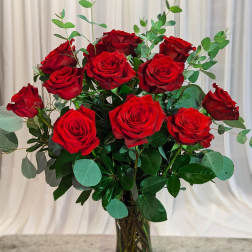 Red roses arranged in a clear glass vase with eucalyptus