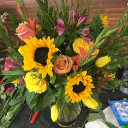 Mixed bouquet with sunflowers, roses, and tulips in a glass vase