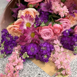 Wrapped bouquet of pink and peach roses with purple and pink blooms on a granite surface