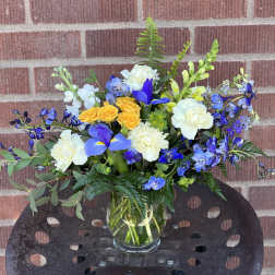 Mixed bouquet of blue, white, and yellow flowers in a glass vase