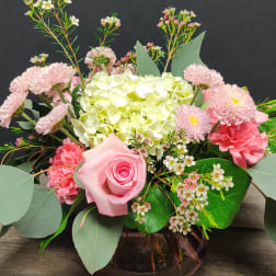 Low arrangement of pink roses, carnations, mums, and white hydrangea in a round glass vase