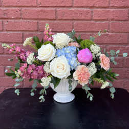 Mixed bouquet in a white vase with white roses, blue hydrangea, and pink blooms