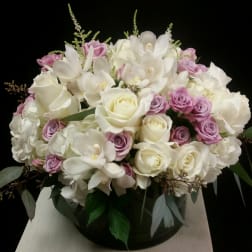 Bouquet of white roses, white orchids, and lavender spray roses in a round vase