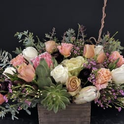 Low arrangement of peach and white roses with protea and succulents in a rustic wooden box