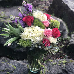 Bouquet of roses, hydrangeas, and purple flowers in a glass vase